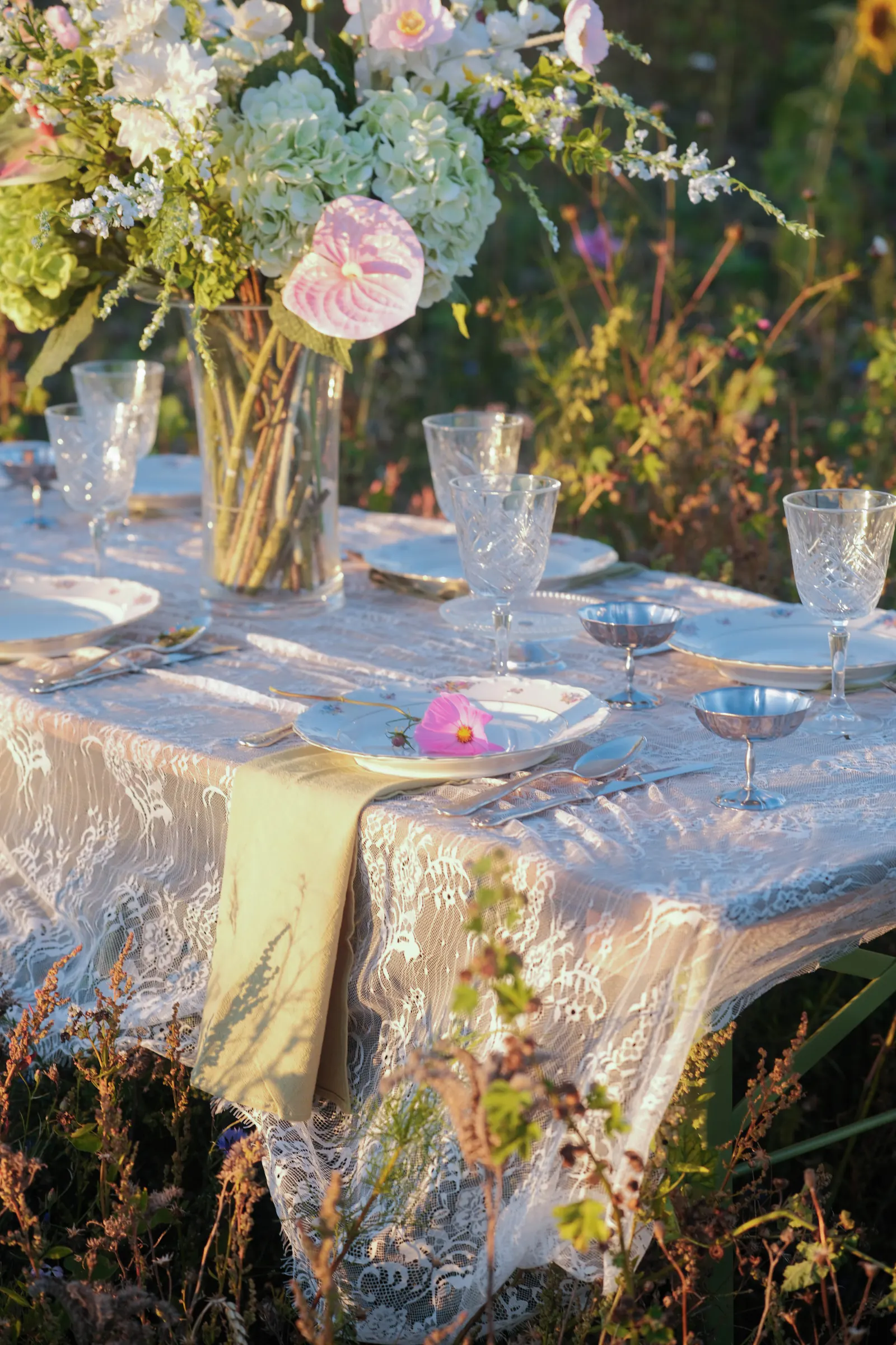 Lange dinertafel met kanten tafellinnen, bloemen en vintage servies